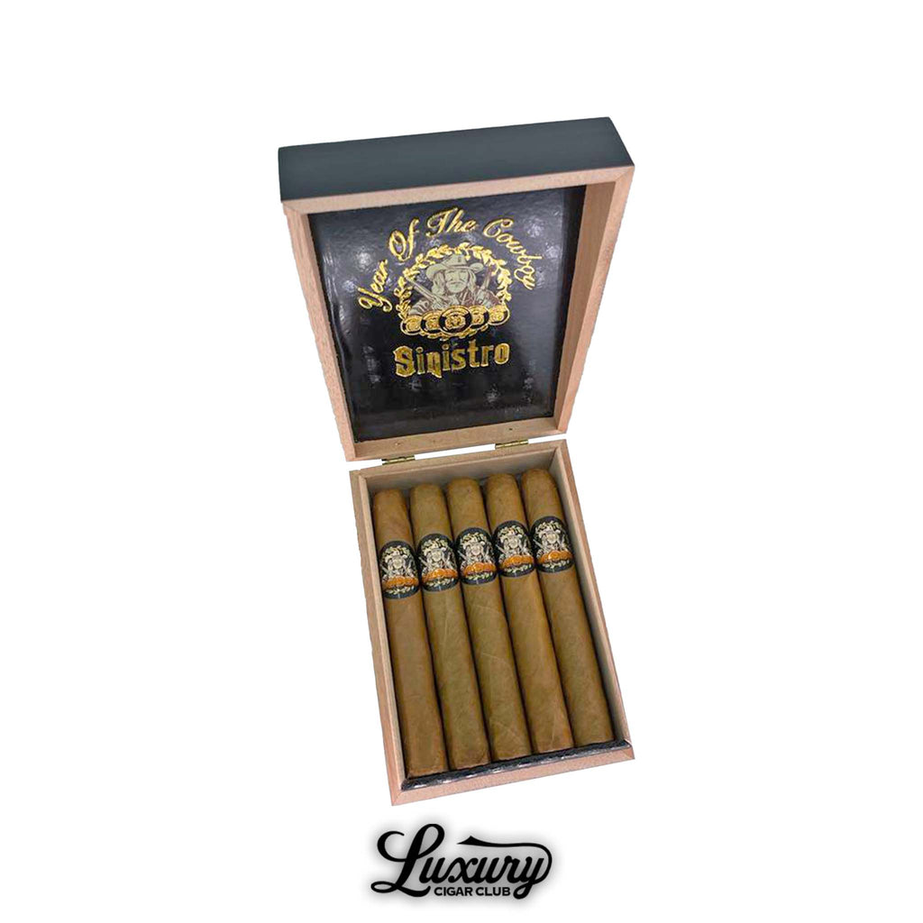 Open wooden box of Sinistro Year of the Cowboy Natural Limited Edition Toro cigars, featuring gold and black artwork on the inside lid with ornate Sinistro logo. Cigars arranged neatly in a single row. Luxury Cigar Club logo displayed below.
