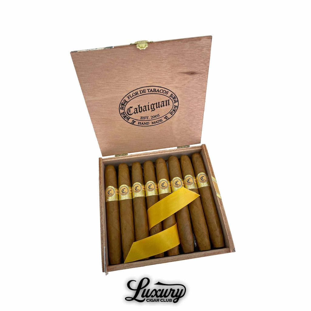 Tatuaje Cabaiguan Británicas Extra cigars displayed in an open cedar box with gold and cream bands, secured with a yellow ribbon, showcasing the elegant handmade presentation, presented by Luxury Cigar Club.