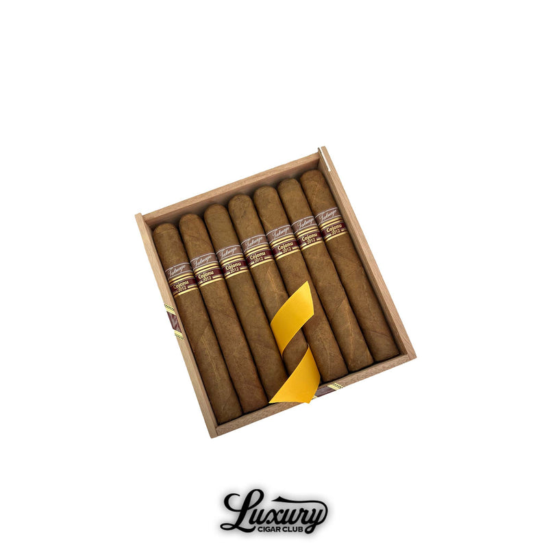 Open wooden box of Tatuaje Cojonu 2012 Corojo cigars wrapped with a yellow ribbon at Luxury Cigar Club