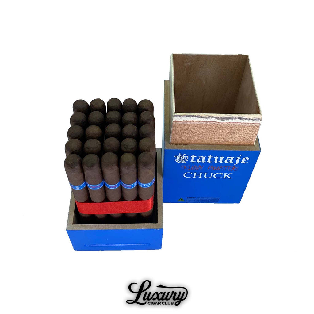 Open box of Tatuaje Skinny Monsters Chuck cigars featuring neatly arranged petit lancero cigars with dark brown wrappers and blue bands, displayed in a bright blue wooden box with the Tatuaje Skinny Monsters Chuck branding, photographed on a white background for Luxury Cigar Club.