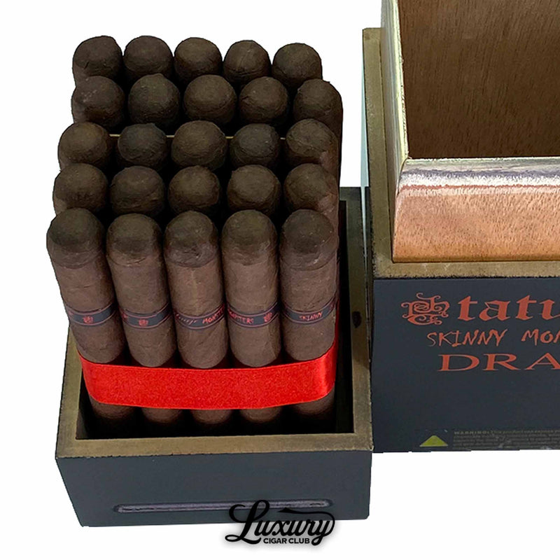 Close-up view of Tatuaje Skinny Monsters Drac Petit Lancero cigars displayed tightly packed with a red ribbon inside the open branded monster-themed box, highlighting the dark Maduro wrappers and black-and-red bands; Luxury Cigar Club product image.