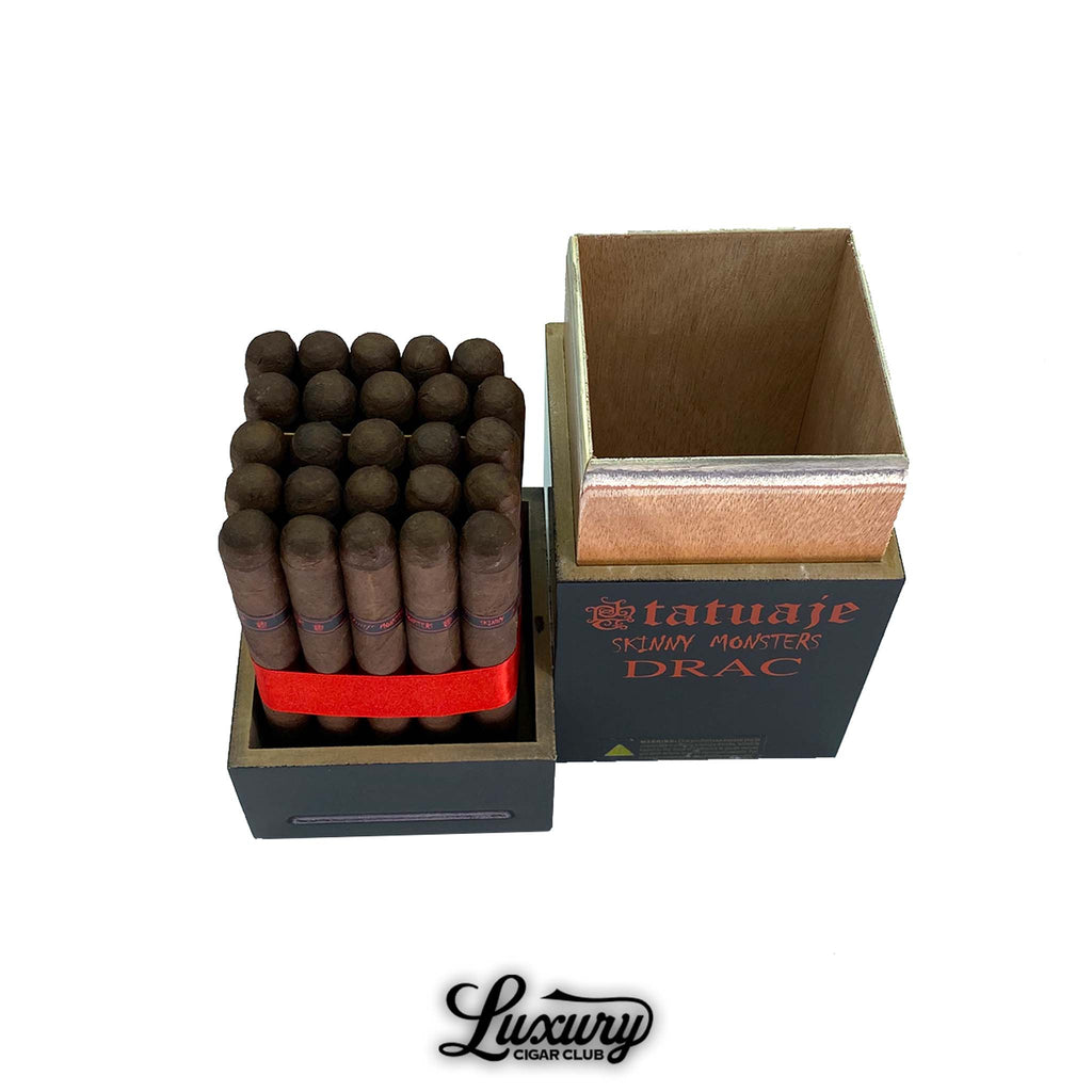 Detailed image of a bundle of Tatuaje Skinny Monsters Drac Petit Lancero cigars arranged upright inside an open black-and-red monster-themed box, with the lid removed and placed beside it; featuring dark brown wrappers, black-and-red cigar bands, and branded packaging; Luxury Cigar Club product photo.