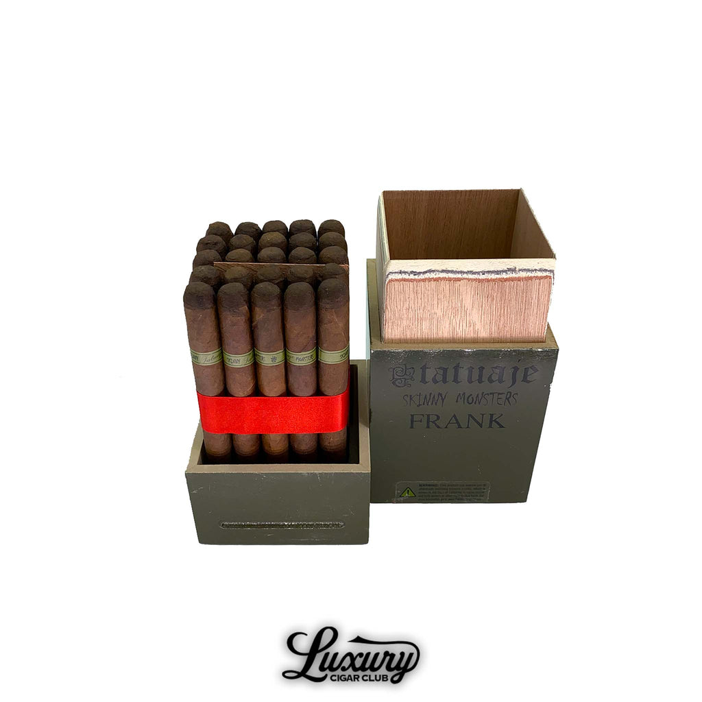 Open olive green Tatuaje Skinny Monsters Frank box showing bundle of slim brown cigars wrapped with red ribbon on the left and the empty box lid on the right, photographed for Luxury Cigar Club.