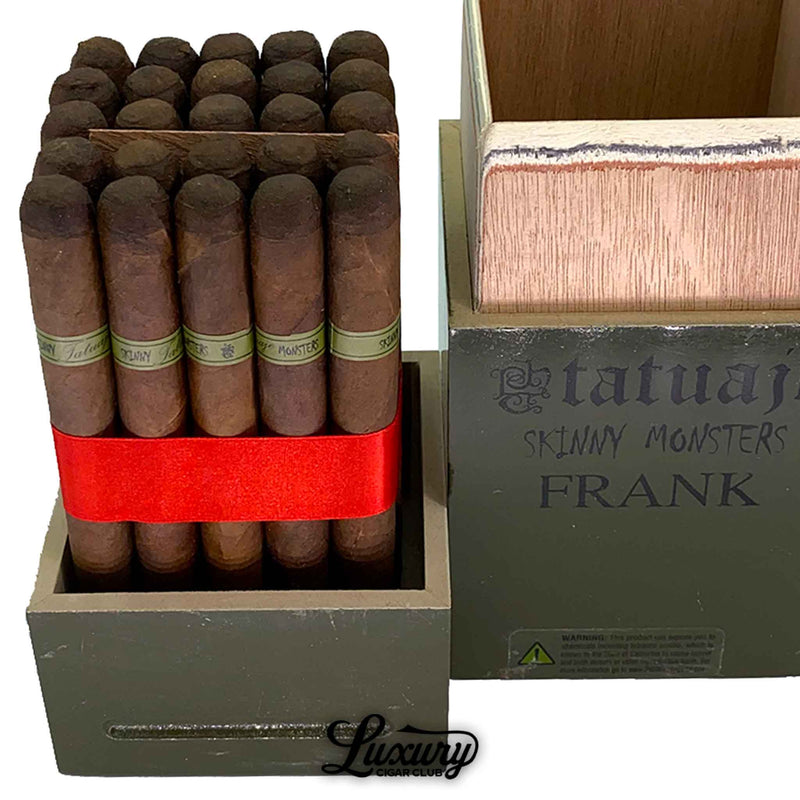 close-up of tatuaje skinny monsters frank petit lancero cigars standing in an olive-green open box, cigars secured with a red ribbon, showing the green frank bands and textured box edges, with the tatuaje skinny monsters frank branding visible on the right section of the container