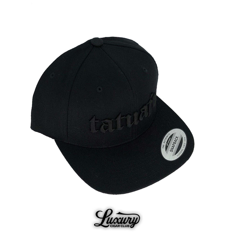 Black Tatuaje snapback hat with embroidered logo shown close up at Luxury Cigar Club.