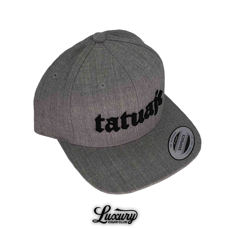 Grey Tatuaje snapback hat with black embroidered logo presented at Luxury Cigar Club.