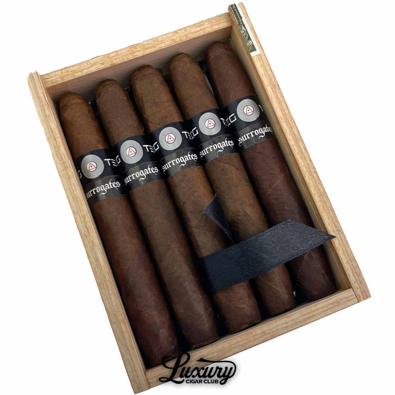 Close-up of Tatuaje Surrogates Big Ten Britanicas Extra cigars in open wooden box showing dark brown wrappers with black Surrogates bands, photographed for Luxury Cigar Club.