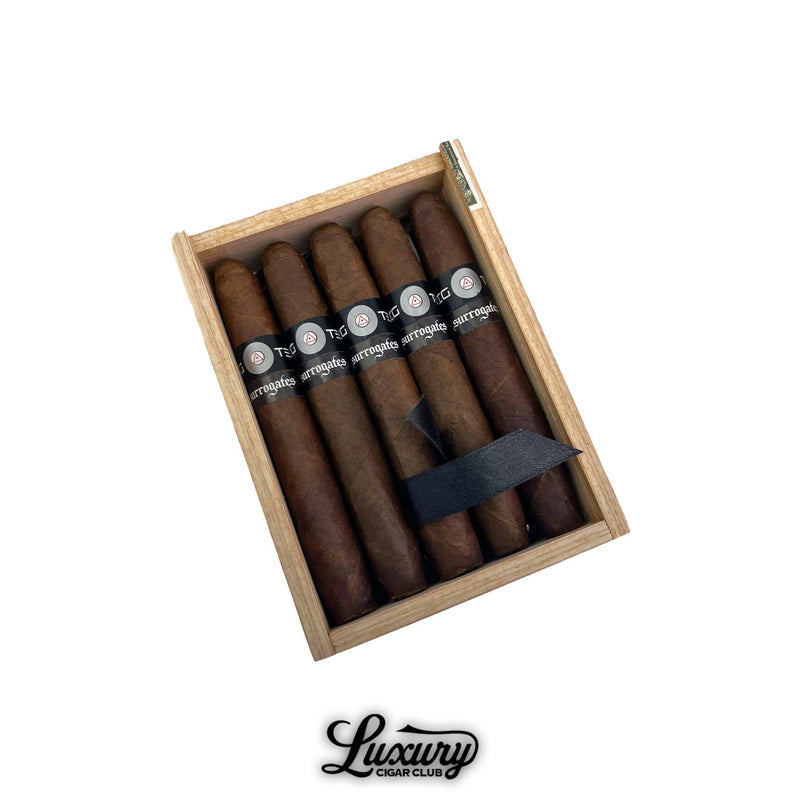 Box of Tatuaje Surrogates Big Ten Britanicas Extra cigars open on white background with black bands and “Surrogates” branding visible, presented for sale by Luxury Cigar Club.