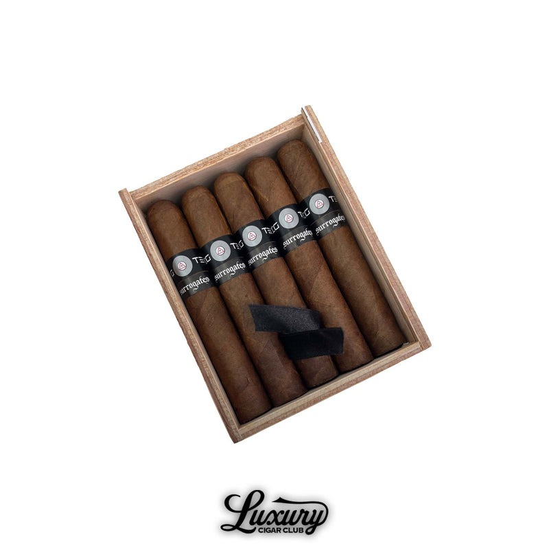 Box of Tatuaje Surrogates Big Ten Robusto cigars open on white background with black Surrogates bands, displayed for Luxury Cigar Club product listing.