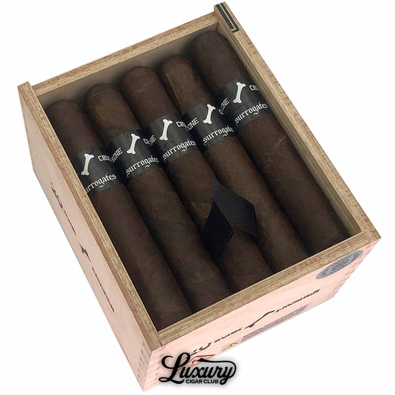 Close up of Tatuaje Surrogates Bone Crusher cigars inside the open wooden box, highlighting the dark wrapper and black Surrogates bone-logo bands with Luxury Cigar Club branding.