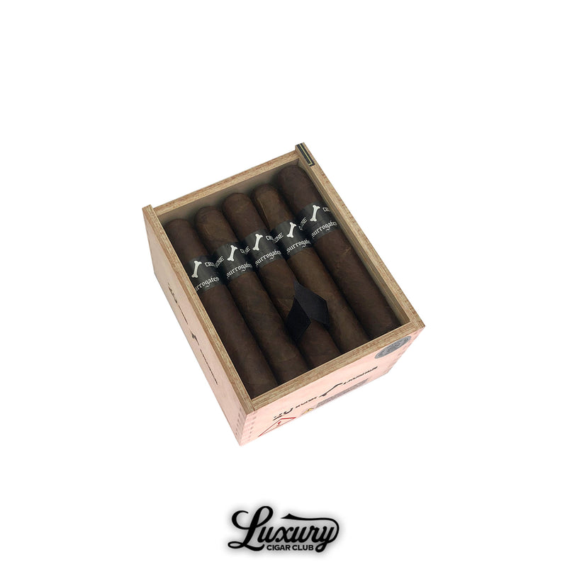 Open wooden box of Tatuaje Surrogates Bone Crusher cigars showing six dark brown robusto cigars with black bands featuring a white bone logo, displayed at an angle on a white background with Luxury Cigar Club branding.