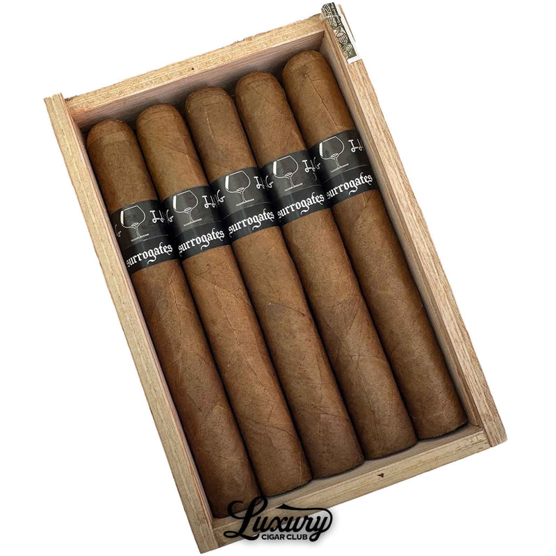 Close up of the open box of Tatuaje Surrogates Closing Time Toro cigars highlighting the cigar construction, wrapper color and black and white Surrogates bands, Luxury Cigar Club branding at bottom.
