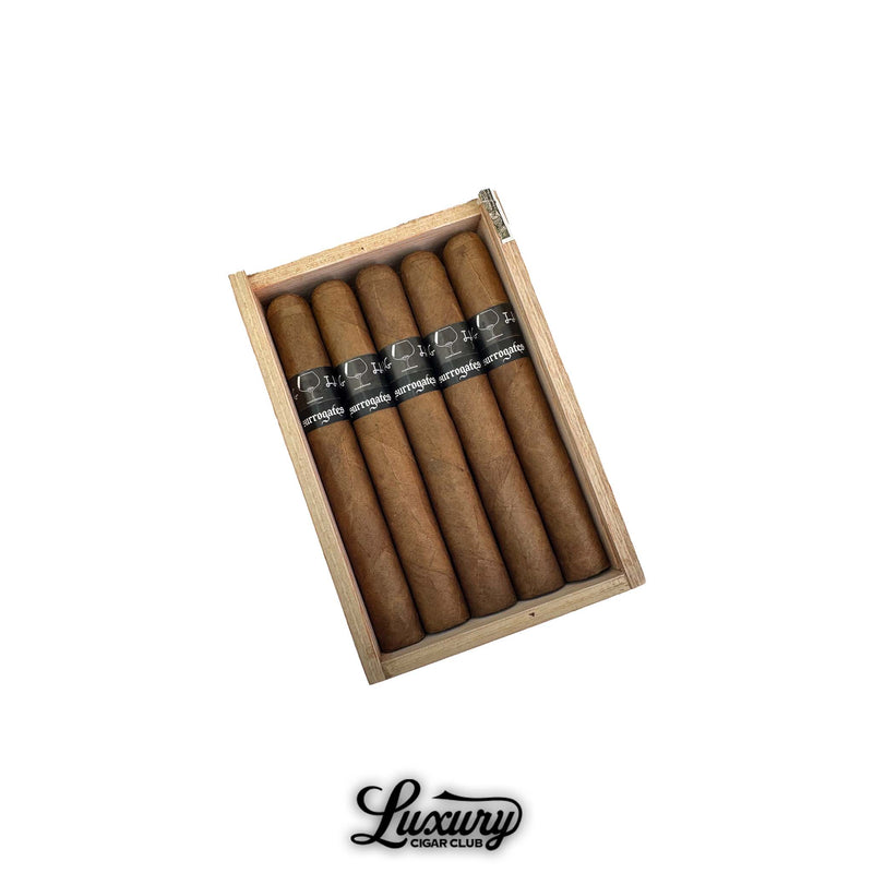 An open cedar box filled with Tatuaje Surrogates Closing Time Toro cigars neatly arranged inside, showing light brown wrappers and black Surrogates bands, Luxury Cigar Club branding at the bottom.