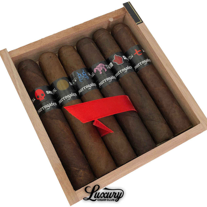 Close-up of Tatuaje Surrogates Sampler Robusto Exclusivos cigars showcasing unique colorful bands in a wooden box, displayed by Luxury Cigar Club.