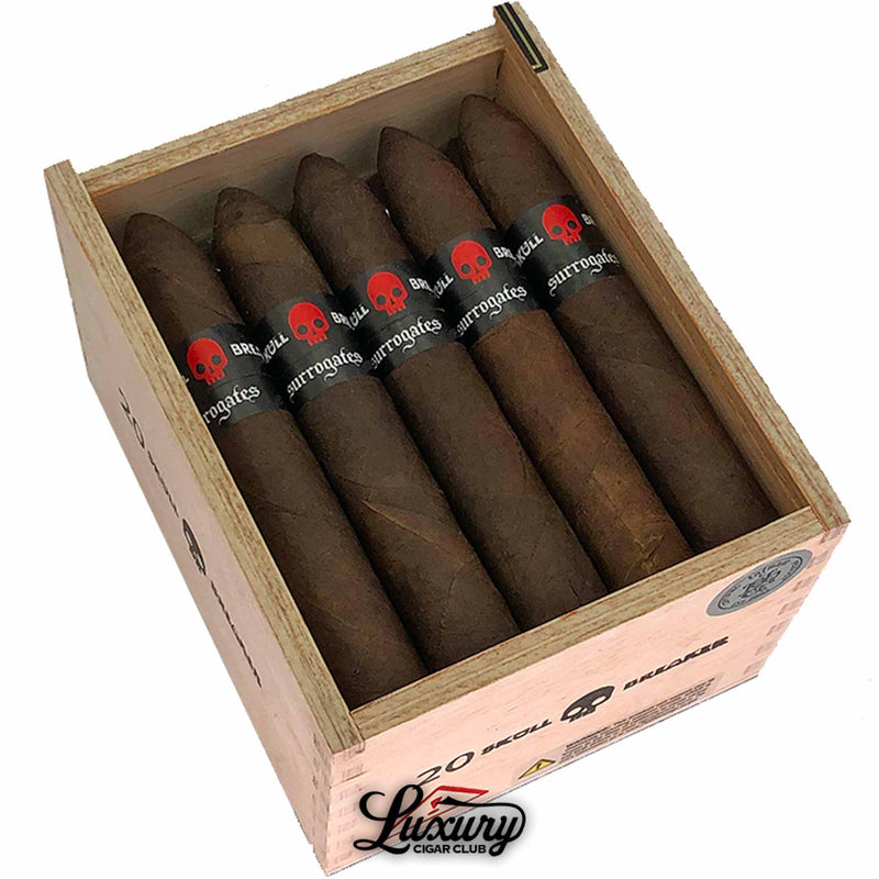 Close up view of Tatuaje Surrogates Skull Breaker Belicoso cigars in a wooden box, showing dark maduro wrappers and bold black bands with red skull artwork, photographed for Luxury Cigar Club.