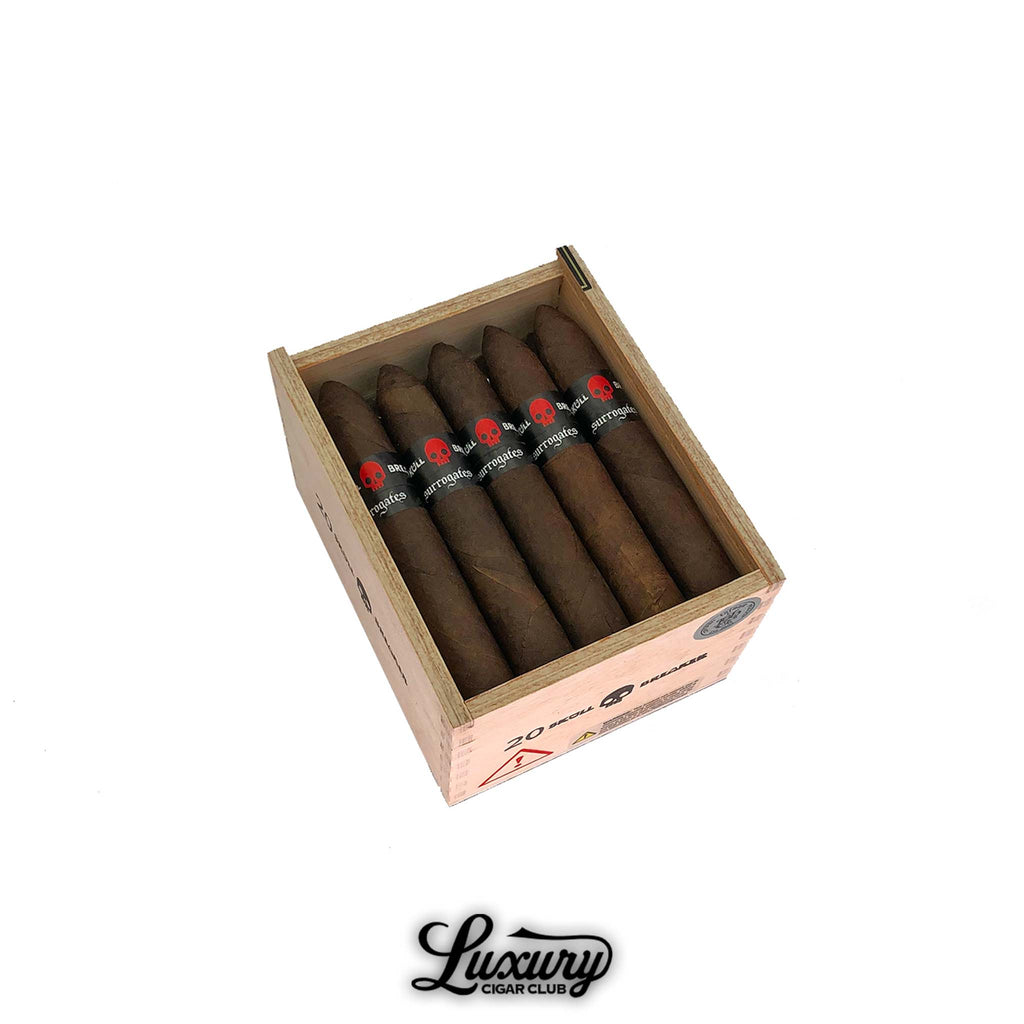 Open cedar box of Tatuaje Surrogates Skull Breaker Belicoso cigars, each wrapped in dark brown tobacco with black bands featuring a red skull, displayed for sale at Luxury Cigar Club.