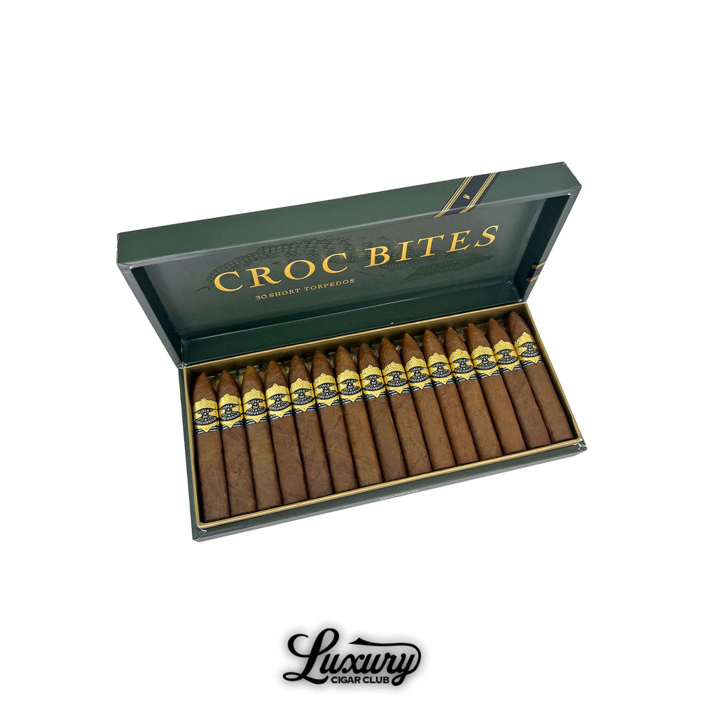 Warped Isla del Cocodrilo Croc Bites open 30-count box showing short torpedo cigars with gold and black bands, premium cigar sampler photographed by Luxury Cigar Club.