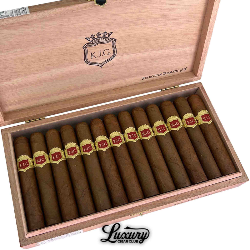 Close up overhead view of Warped Selección Domain 4546 cigars inside the wooden box, highlighting the brown wrapper leaves and red and gold KJG cigar bands, Luxury Cigar Club logo visible below.