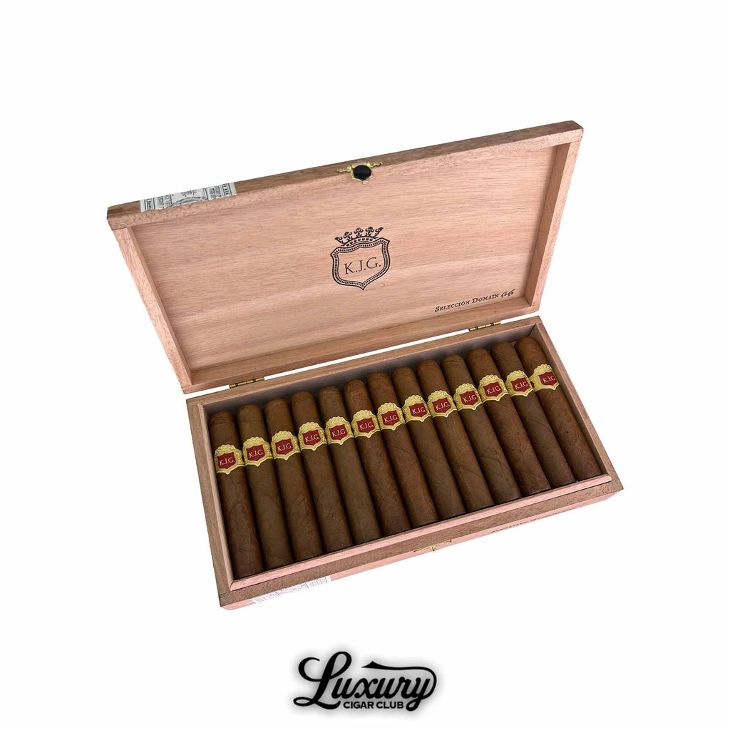 Open wooden box of Warped Selección Domain 4546 cigars angled on white background, showing a full row of cigars with red and gold KJG bands and the Luxury Cigar Club logo underneath.