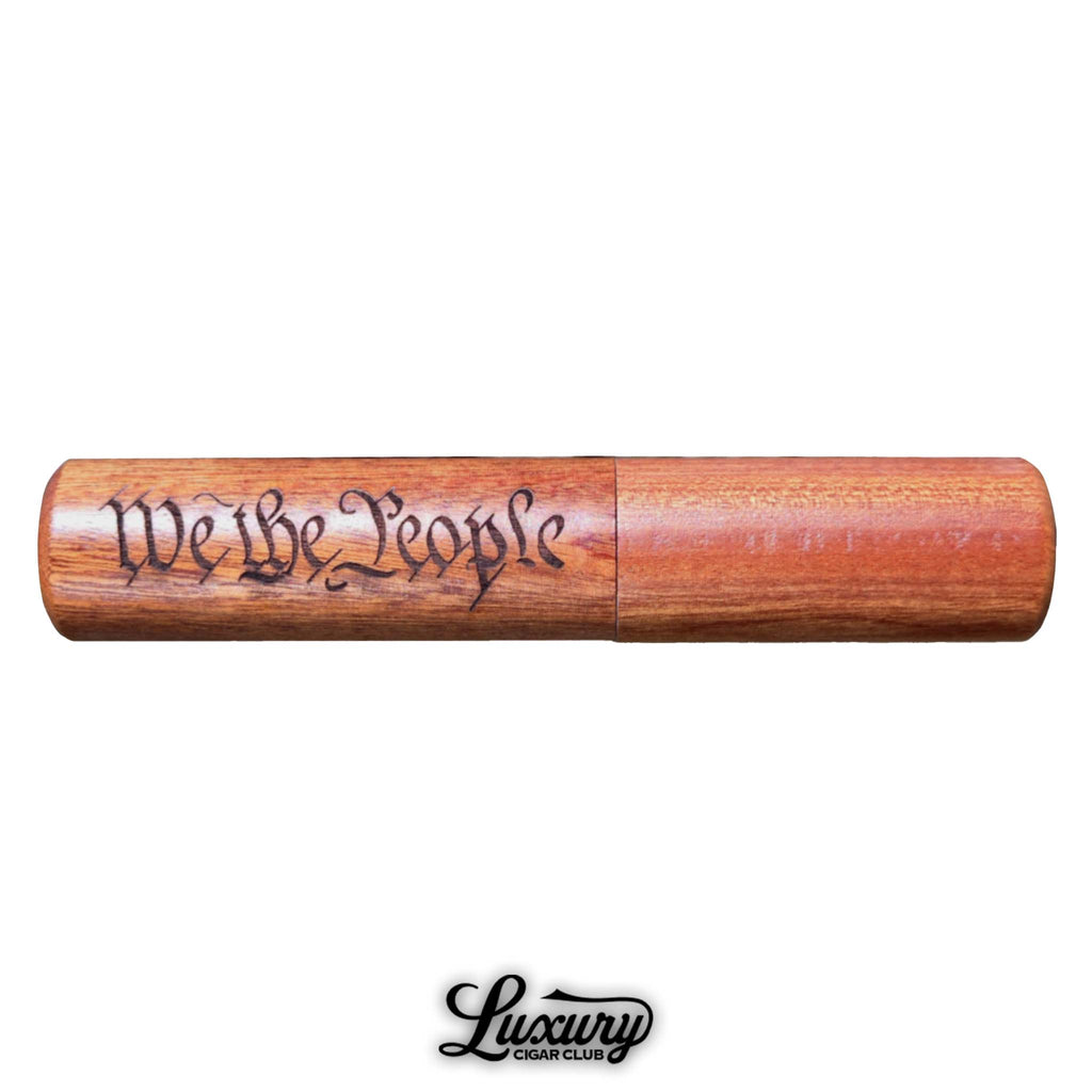 Wooden cigar holder engraved with the phrase "We the People" in a calligraphic font, featuring a polished finish and cylindrical design. Displayed with the Luxury Cigar Club logo beneath it on a white background.
